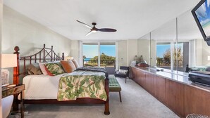 Ein Schlafzimmer mit Bett, Schreibtisch, Stuhl, Deckenventilator und großen Fenstern mit Meerblick.