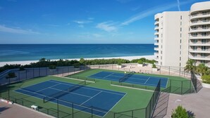 Ein Strandhotel mit mehreren Tennisplätzen, einem Pool und Meerblick.
