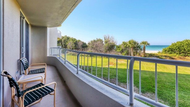 Ein Balkon mit zwei Stühlen und Blick auf den Strand, unter einem klaren Himmel.