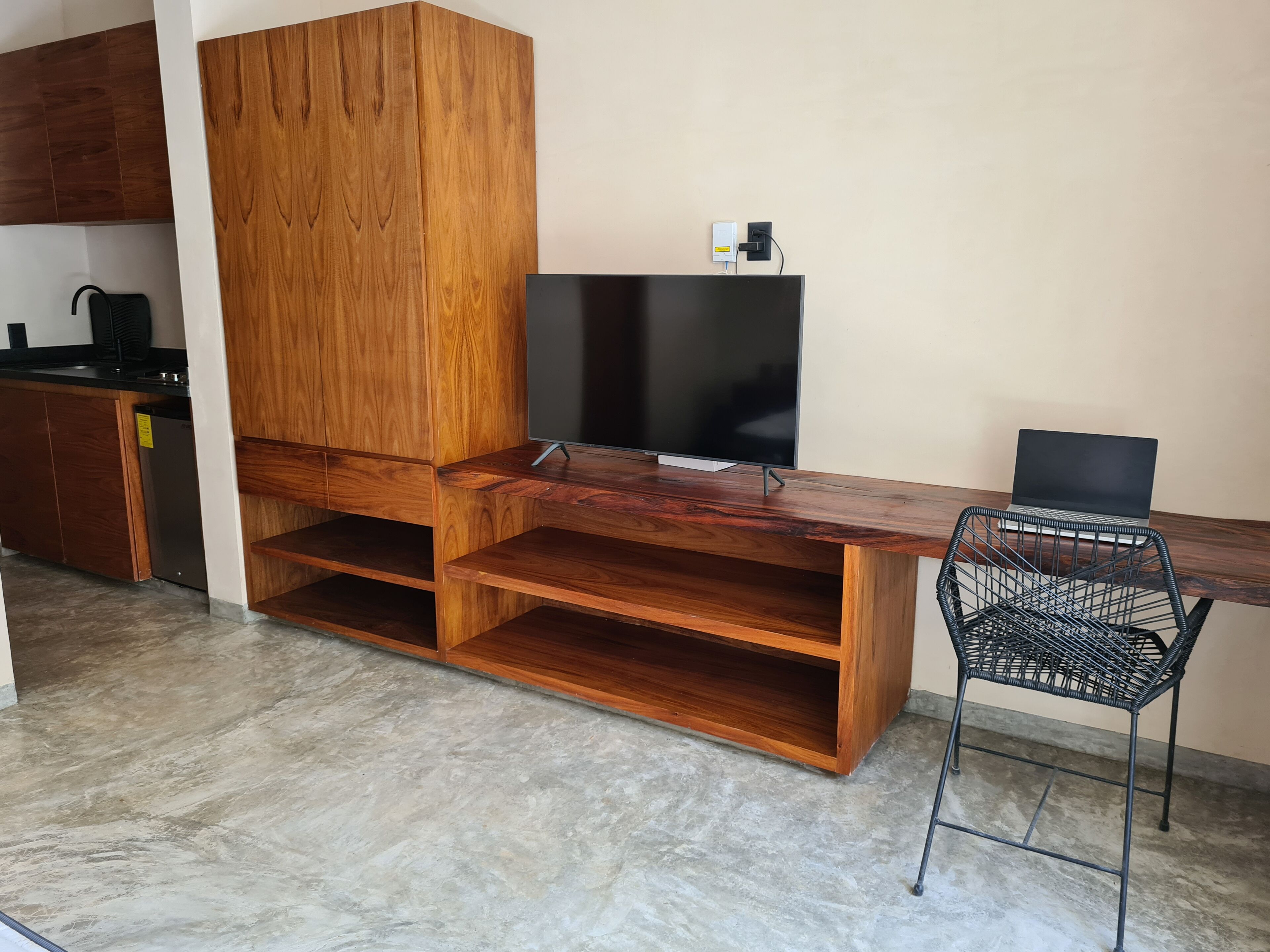 A modern kitchen with wooden cabinets, a built-in TV, and a laptop on a desk.