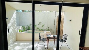A modern room with a sliding glass door leading to a balcony with a table and chairs, a small seating area, and a view of the outdoors. - Private Jacuzzi with Pool  Studio S11 (Tulum)
