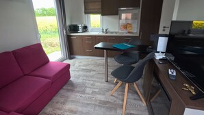 En kompakt opholdsstue med sofa, spisebord med stole, et tekøkken og et fjernsyn.