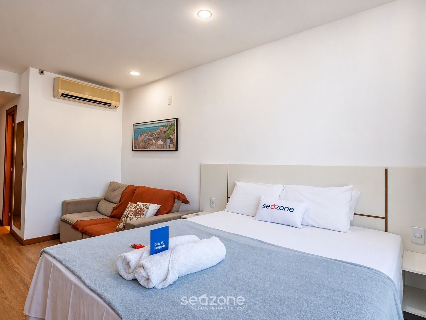 Una habitación de hotel con cama, sofá, aire acondicionado y un cuadro en la pared.
