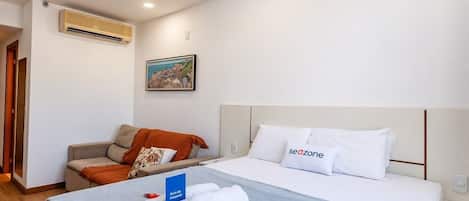 Una habitación de hotel con cama, sofá, aire acondicionado y un cuadro en la pared.