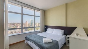 A hotel room with a large window, a bed with white linens, a grey blanket, and a white pillow. - Your Complete Stay in a Building With Pool and Gym, 290m From Shopping da Bahia - Ibfs (Salvador)