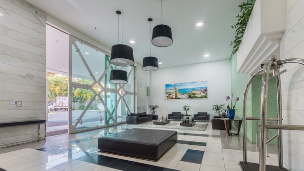 A modern lobby with a black leather sofa, a coffee table, and a painting of a coastal scene. - Your Complete Stay in a Building With Pool and Gym, 290m From Shopping da Bahia - Ibfs (Salvador)