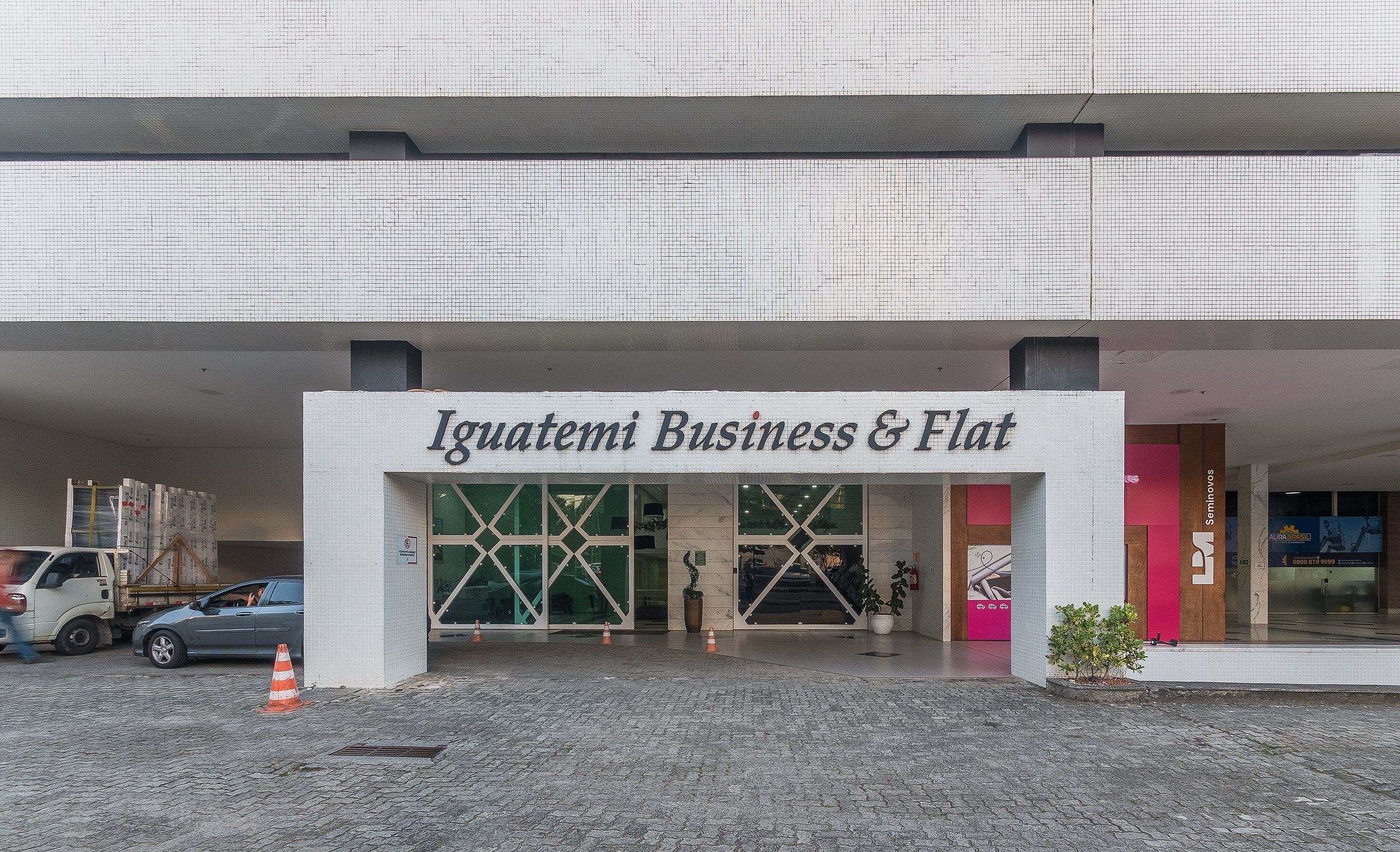 The entrance to Iguatemi Business & Flat with a paved area, a truck, and a car parked outside.