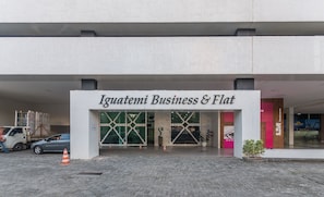Indgangen til Iguatemi Business & Flat med et belagt område, en lastbil og en bil parkeret ude foran.