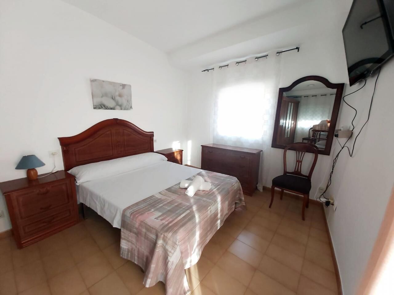 A bedroom with a bed, a dresser, a chair, a TV, and a window.