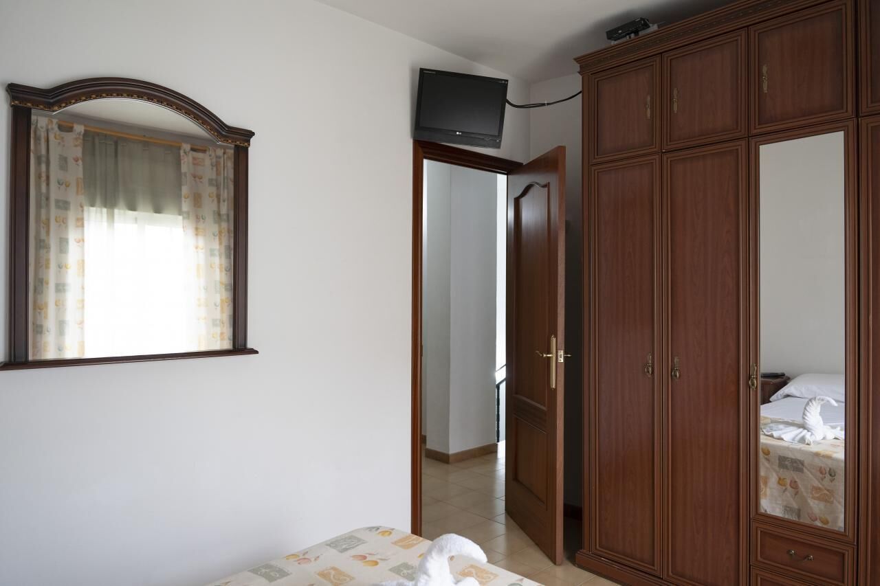Un dormitorio con cama, armario, espejo y televisor en la pared.