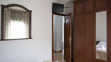 Un dormitorio con cama, armario, espejo y televisor en la pared.
