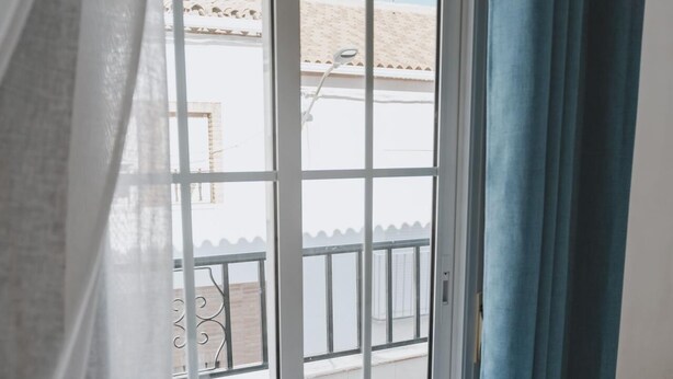Een hotelkamer met een bed, een raam met gordijnen en uitzicht op een balkon.