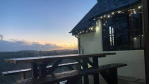 An outdoor seating area with picnic tables and string lights, overlooking a scenic view. - Pirates Inn Themed 3 bedroom cottage, with bar & pool table (Tregaron)