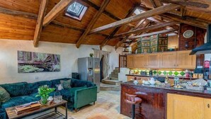 A rustic interior with a stone floor, wooden beams, a green sofa, a kitchen area with wooden cabinets, and a staircase leading to an upper level. - Pirates Inn Themed 3 bedroom cottage, with bar & pool table (Tregaron)