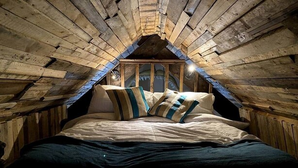 A cozy attic bedroom with a sloped ceiling, a bed with striped bedding, and a rustic wooden interior. - Pirates Inn Themed 3 bedroom cottage, with bar & pool table (Tregaron)