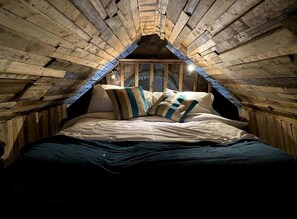 A cozy attic bedroom with a sloped ceiling, a bed with striped bedding, and a rustic wooden interior. - Pirates Inn Themed 3 bedroom cottage, with bar & pool table (Tregaron)