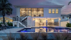 Een modern huis met twee verdiepingen, voorzien van een zwembad, buitenmeubilair en een trap naar een balkon.