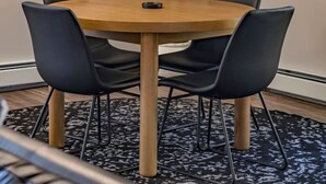 A conference room with a round wooden table, black chairs, and a large artificial tree. - The Pine Street Inn - Room 5 (Watertown)