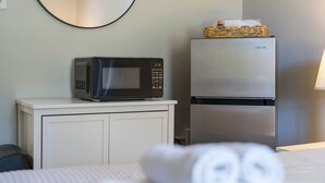 A hotel room with a microwave on a small table, a refrigerator, and a bed with rolled towels. - The Pine Street Inn - Room 1 (Watertown)