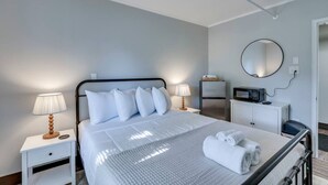 A hotel room with a bed, bedside tables, a desk, a microwave, a refrigerator, and a mirror. - The Pine Street Inn - Room 3 (Watertown)