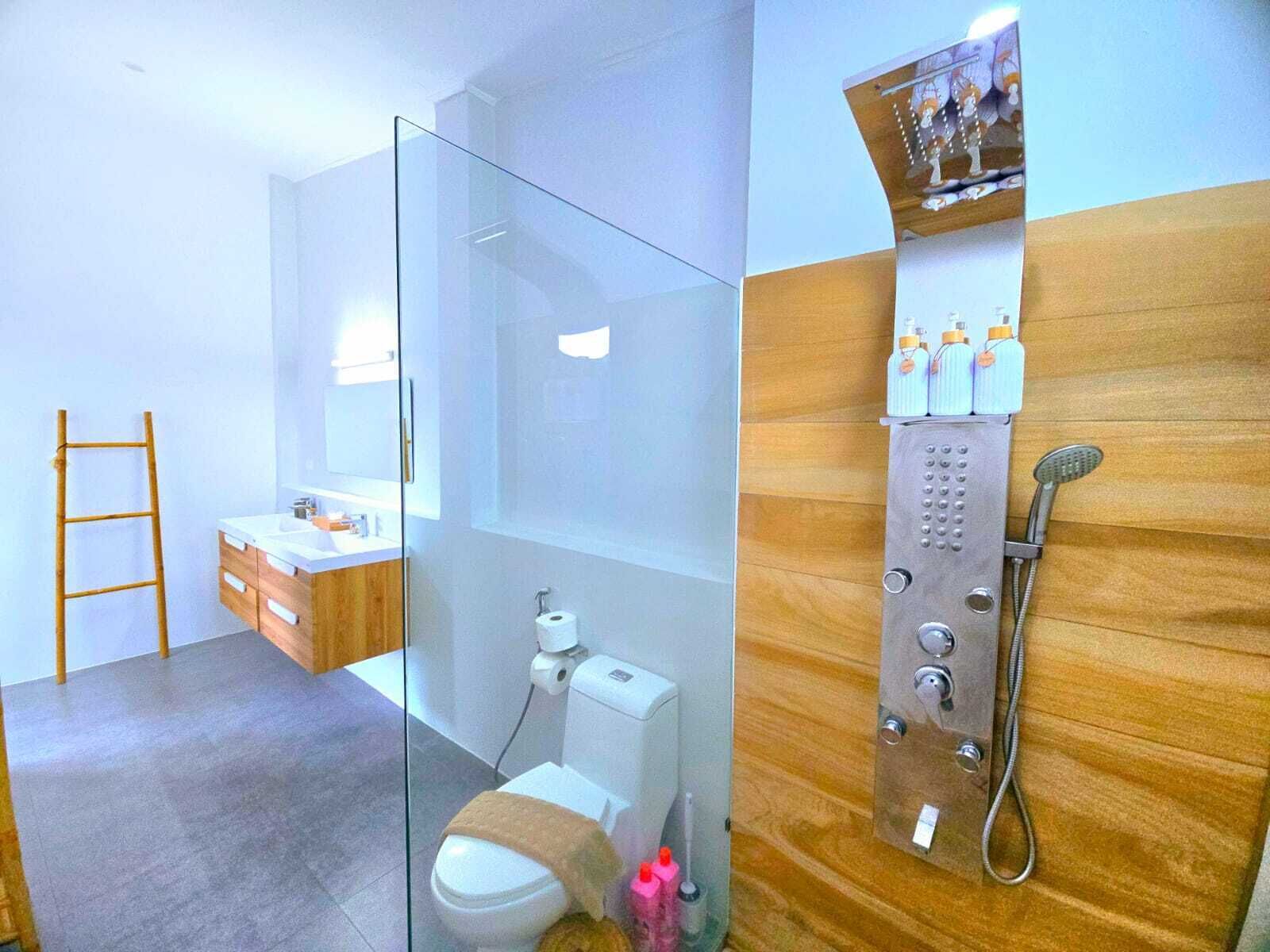 A modern bathroom with a glass shower enclosure, a wooden vanity, and a toilet with a towel on it.