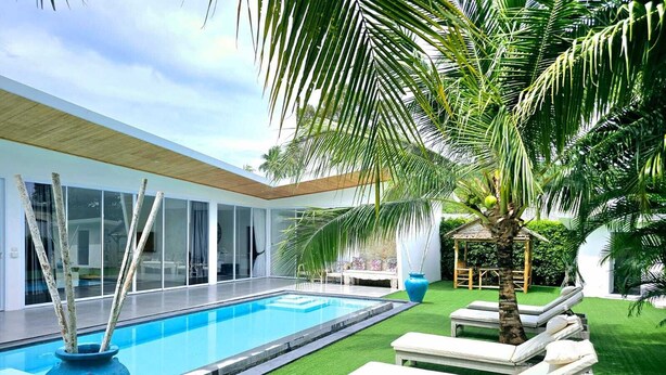 Un espace piscine moderne avec une piscine à l’eau d’un bleu limpide, de l’herbe artificielle verte et des chaises longues.