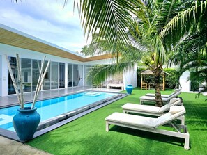 Un espace piscine moderne avec une piscine à l’eau d’un bleu limpide, de l’herbe artificielle verte et des chaises longues.