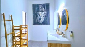 Une salle de bain avec une échelle en bois, un grand tableau représentant Bouddha, un lavabo blanc et un miroir avec un cadre doré.