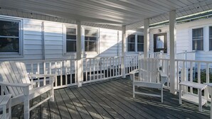 Une véranda couverte avec des balustrades blanches et une terrasse en bois.