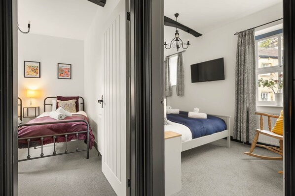 A bedroom with two beds, a TV, a chandelier, and a window with curtains. - Period Cottage Settle (Settle)