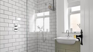 A bathroom with white subway tiles, a shower, a sink with a mirror, and a window. - Period Cottage Settle (Settle)