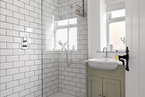 A bathroom with white subway tiles, a shower, a sink with a mirror, and a window. - Period Cottage Settle (Settle)