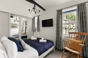 A hotel room with a bed, a wooden rocking chair, a TV, and a window with curtains. - Period Cottage Settle (Settle)