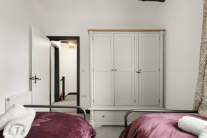 A bedroom with two beds, a wardrobe, and a hallway leading to a bathroom. - Period Cottage Settle (Settle)