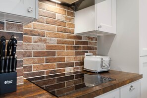 A kitchen with a brick backsplash, a toaster, and a knife block. - Period Cottage Settle (Settle)