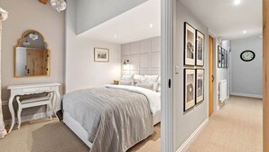 Une chambre à coucher avec un lit, une table de chevet et un miroir. Il y a un tableau encadré au mur et une horloge accrochée au mur.