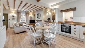 Une cuisine moderne avec des armoires blanches, un comptoir en bois et un four encastré. On y trouve également un coin repas avec une table ronde et des chaises blanches.