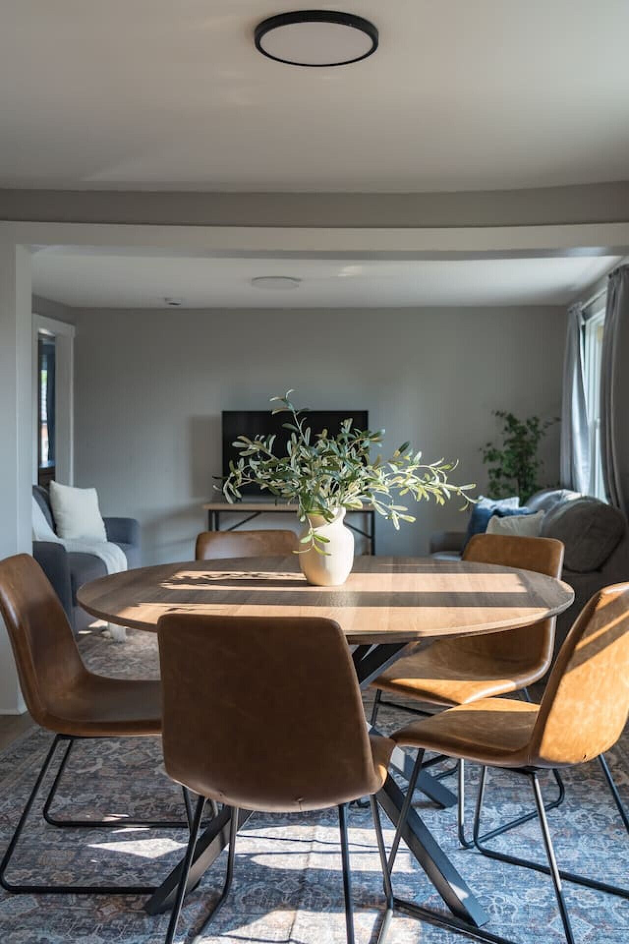 A modern dining area with a round wooden table, brown upholstered chairs, and a potted plant.