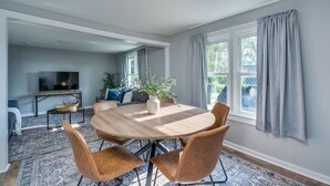 Un coin repas avec une table ronde, quatre chaises, une plante en pot et un téléviseur en arrière-plan.