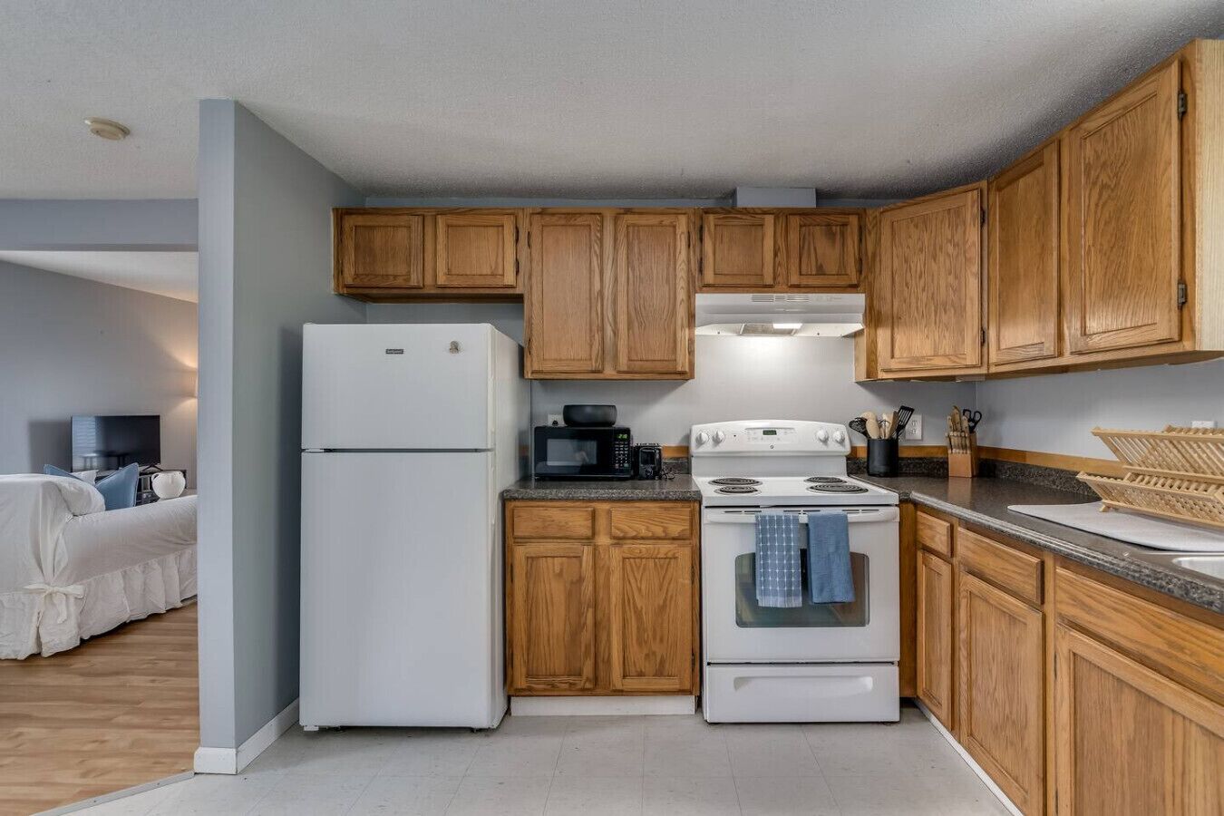 A compact kitchen with wooden cabinets, a white refrigerator, a microwave, and a stove.