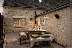 Ein Steinhaus mit einer Terrasse, einem Tisch mit Stühlen und einer Bank mit Kissen.