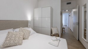 Un dormitorio con cama, armario, silla y un pasillo que conduce a otra habitación.