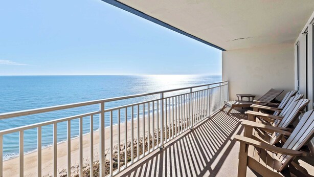 Een balkon met uitzicht op de oceaan, houten stoelen en een leuning.