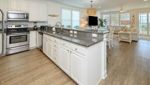 Una cocina con armarios blancos, encimera de granito, electrodomésticos de acero inoxidable y un comedor con sofá y mesa blancos.