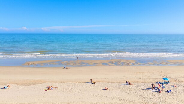 Una playa con gente tomando el sol y nadando.