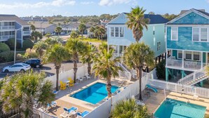 Zona residencial con piscina rodeada de palmeras y una casa de dos pisos con balcón.