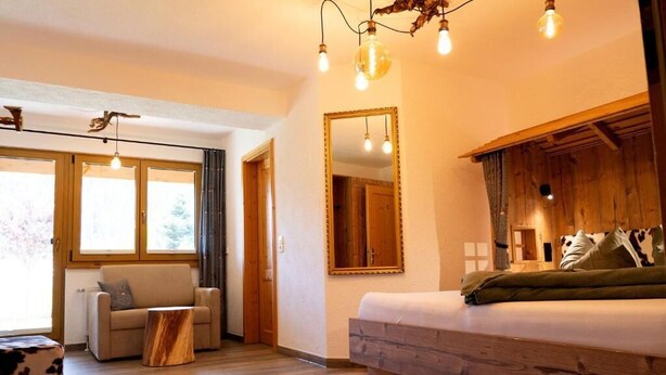 Una habitación acogedora con una cama de madera, un sofá y una mesita. Hay un espejo grande en la pared y una ventana con cortinas.