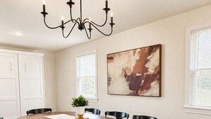 Een eetkamer met een grote ovale tafel, zwarte stoelen, een kroonluchter en een schilderij aan de muur.