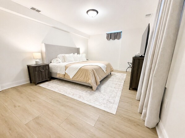 A bedroom with a bed, nightstand, and a large window with curtains.
