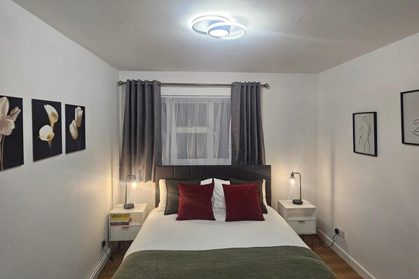 A bedroom with a bed, two bedside tables, a window with curtains, and wall art. - 1 Bed Flat - Sleeps 4 - Pets - Parking - Wifi (London)
